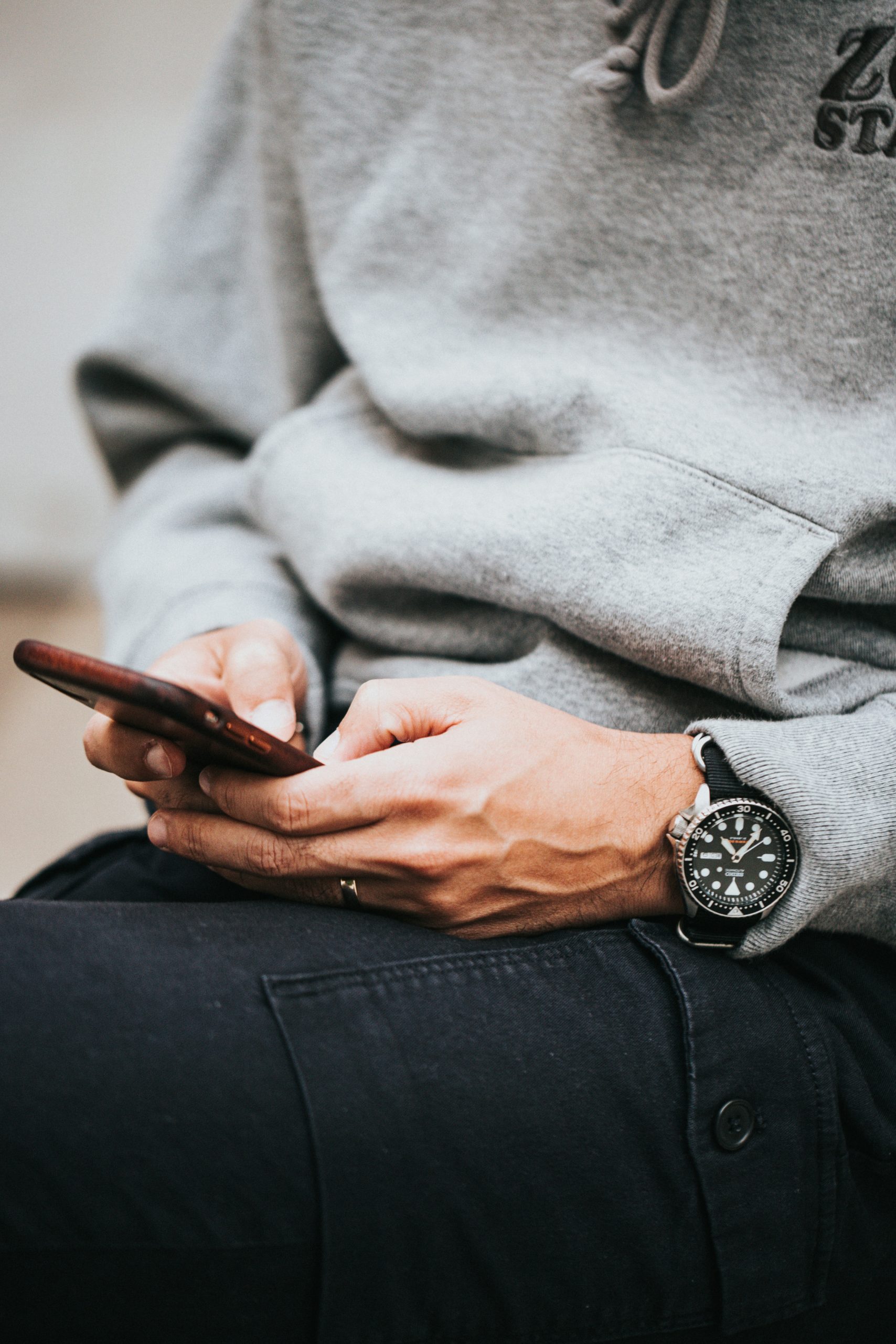 Person in gray hoodie using smartphone, illustrating mobile engagement for direct mail solutions in law firms